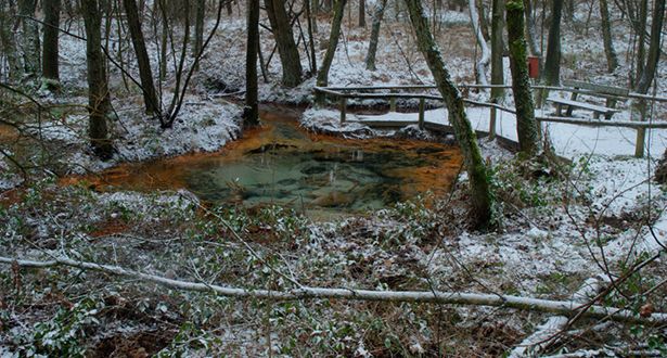 Schneebedeckte Schwindequelle mit rötlichen und türkisfarbenen Ablagerungen
