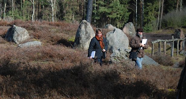 Zwei Spaziergänger gehen durch die Heidefläche an Steindenkmälern vorbei