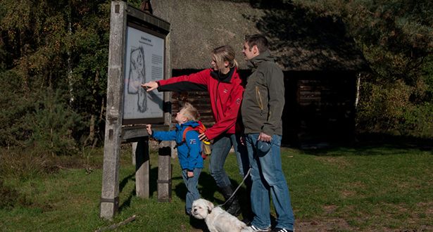 Mutter, Vater, Sohn und Hund stehen vor einem Wegweiserplakat