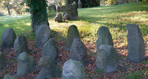 Bildausschnitt eine Gruppe von Steindenkmälern auf einer grünen Wiese und von Blattlaub umgeben