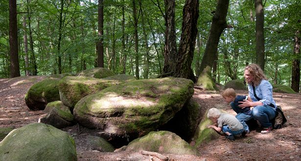 Eine Frau und zwei kleine Jungen schauen hinunter in die dunkle Höhle eines Steingrabs