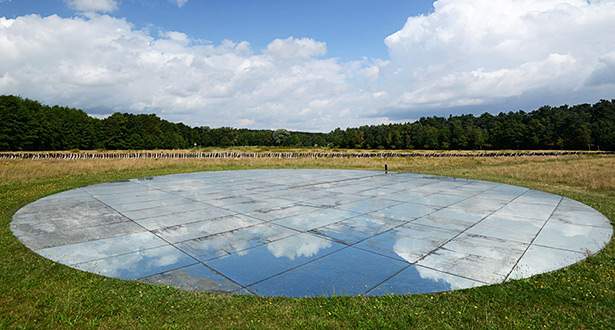 Spiegelartiges, flaches und kreisrundes Kunstwerk aus Glas auf einer Wiese.